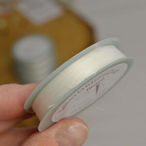 a hand holding a spool of white thread