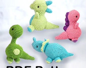 May include: Four crocheted dinosaur toys in different colours: green, light green, pink, and blue. The dinosaurs are sitting on a white surface. PDF Pattern.