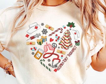 May include: Ivory-colored t-shirt featuring a heart-shaped design filled with medical and Christmas-themed illustrations. The design includes a stethoscope, lungs, a Christmas tree, and the text "Respiratory Therapist".