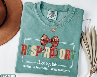 May include: Light green t-shirt with the words "RESPIRATORY therapist" in red and green letters, a bow tie, and a stethoscope graphic. The shirt also has the text "BREATHE IN POSITIVITY, EXHALE NEGATIVITY".