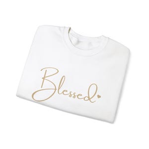 May include: White t-shirt with the word "Blessed" written in gold cursive script.