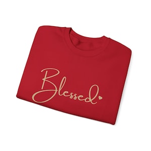 May include: Red t-shirt with the word "Blessed" written in gold script with a small heart next to it.