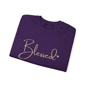 May include: Purple t-shirt with the word "Blessed" in gold script with a small gold heart.