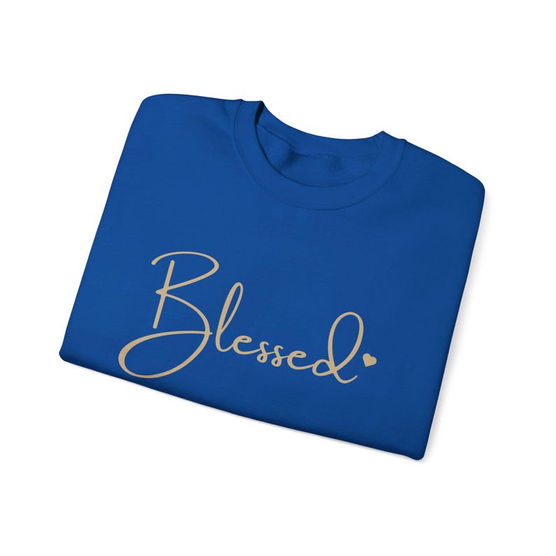 May include: A royal blue t-shirt with the word "Blessed" written in a cursive font in a light beige color. A small heart is to the right of the word.