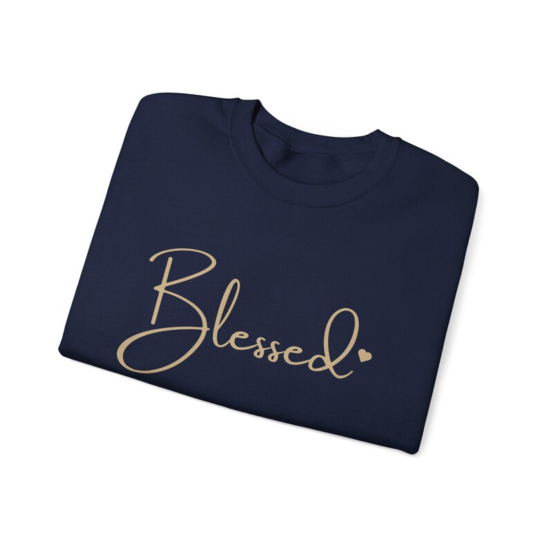May include: A navy blue t-shirt with the word "Blessed" written in a cursive font in gold. A small gold heart is to the right of the word.