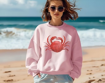 May include: A pink sweatshirt with a red watercolor crab design. The sweatshirt has long sleeves and a crew neck.