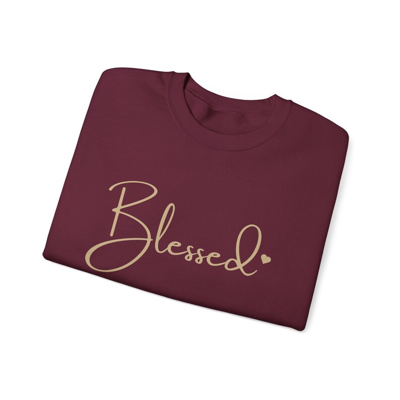 May include: Burgundy t-shirt with the word "Blessed" written in a cursive font in gold with a small heart after the word.