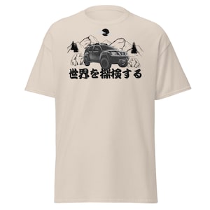 May include: A beige t-shirt with a black graphic of a car driving through a mountain landscape. The text "世界を征服する" is printed below the graphic.