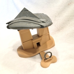 May include: A 3D-printed model of a futuristic structure, featuring a gray, segmented top and tan-colored base with architectural details. A separate ring-shaped piece is also included. The model is designed with intricate patterns and textures.