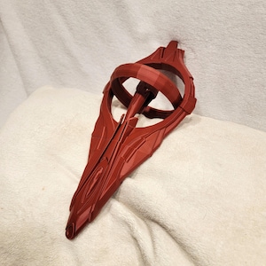 May include: A dark red, 3D-printed, pointed, elongated object with a central circular ring structure. The surface features geometric, angular paneling and a smooth, matte finish, creating a complex, symmetrical, and futuristic-looking design.