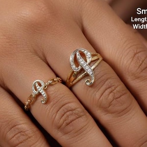 Pode incluir: Dois anéis dourados com a letra "P" adornada com pequenas pedras transparentes. O anel maior tem 19 mm de comprimento e 16 mm de largura. O anel menor tem 19 mm de comprimento e 11 mm de largura.