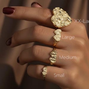 May include: A hand displays four gold-colored rings of varying sizes: XX-Large, Large, Medium, and Small. Each ring features a textured, nugget-like design. The rings are set against a neutral background.