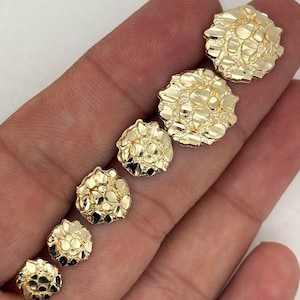 Op de afbeelding: Zes goudkleurige nugget-oorbellen van verschillende maten worden getoond. De oorbellen hebben een getextureerd, onregelmatig oppervlak en zijn diagonaal gerangschikt. Ze staan op een lichte achtergrond.