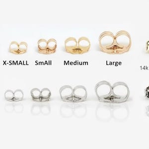 May include: An assortment of gold and silver earring backs in various sizes, labeled X-SMALL, SmAll, Medium, and Large. The text "14k Stamped" is also visible. The earring backs are displayed on a white surface.