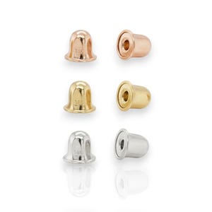 May include: Six earring backs in various metallic finishes: rose gold, gold, and silver. Each back is a small, rounded shape with a hole for the earring post. The backs are arranged in two rows of three against a white background.