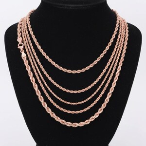 K&ouml;nnte beinhalten: Eine Sammlung von Halsketten mit Seilkette in Ros&eacute;gold, pr&auml;sentiert auf einer schwarzen Mannequin-B&uuml;ste. Die Halsketten variieren in der L&auml;nge und zeigen einen mehrschichtigen Look. Die Ketten haben ein gedrehtes Seildesign und einen Karabinerverschluss.
