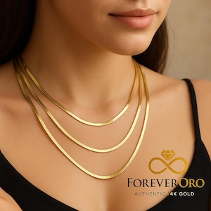 May include: Three gold herringbone necklaces layered on a person's neck. The necklaces are a bright yellow gold colour and lay flat against the skin. The image includes the text "FOREVER ORO AUTHENTIC 14K GOLD" in a gold diamond logo.