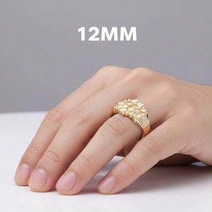 Puede incluir: Un anillo dorado con un dise&ntilde;o de racimo, de 12 mm, se muestra en una mano. El anillo tiene una superficie texturizada y una banda rectangular. El fondo es de color s&oacute;lido y neutro.