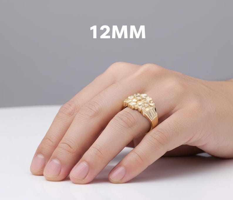 Puede incluir: Un anillo dorado con un dise&ntilde;o de racimo, de 12 mm, se muestra en una mano. El anillo tiene una superficie texturizada y una banda rectangular. El fondo es de color s&oacute;lido y neutro.