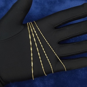 May include: Close-up of several delicate gold-colored twisted rope chains. The chains are displayed on a black surface, with a blue background. The chains are thin and appear to be made of metal, possibly gold or gold-plated.