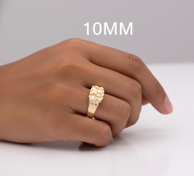 Puede incluir: Un anillo dorado con un dise&ntilde;o texturizado en forma de pepita. El anillo se muestra en una mano, con el texto "10MM" en blanco encima.
