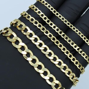 May include: A collection of gold-colored curb chain necklaces of varying widths. The chains are displayed on a black surface, showcasing their different link sizes and overall shine. The chains are a classic jewelry style.