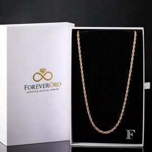 K&ouml;nnte beinhalten: Eine goldene Seilkette, pr&auml;sentiert in einer offenen wei&szlig;en Schachtel mit schwarzem Innenraum. Auf der Schachtel befinden sich das Logo und der Text "ForeverOro". Die Halskette ist mittig in der Schachtel platziert.