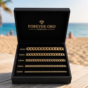 Puede incluir: Una caja de joyer&iacute;a negra con el logotipo de Forever Oro Jewelry, abierta para revelar cinco collares de cadena dorada de diferentes anchos: 2,5 mm, 3,5 mm, 4,5 mm, 5,5 mm y 6,5 mm. La caja est&aacute; sobre una superficie de madera con una playa y un oc&eacute;ano de fondo.