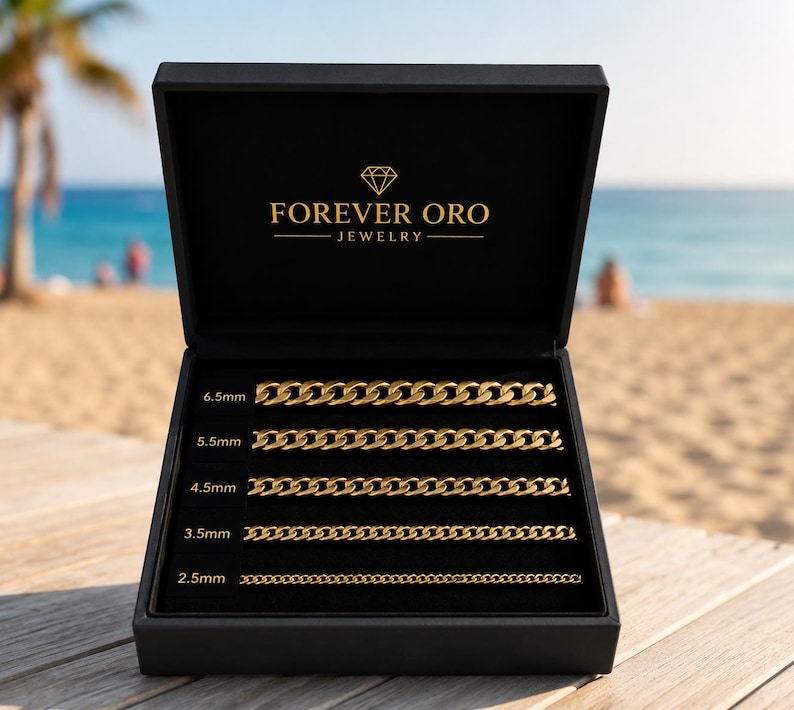 Puede incluir: Una caja de joyer&iacute;a negra con el logotipo de Forever Oro Jewelry, abierta para revelar cinco collares de cadena dorada de diferentes anchos: 2,5 mm, 3,5 mm, 4,5 mm, 5,5 mm y 6,5 mm. La caja est&aacute; sobre una superficie de madera con una playa y un oc&eacute;ano de fondo.