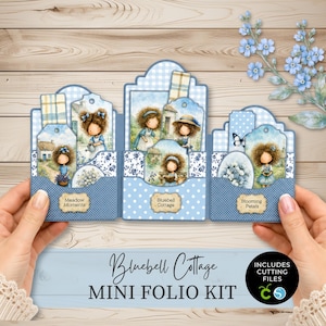 May include: A blue and white paper craft mini folio kit featuring illustrations of girls in garden settings. The kit includes three pockets with tags labelled Meadow Moments, Bluebell Cottage, and Blooming Petals, plus text reading Bluebell Cottage MINI FOLIO KIT and INCLUDES CUTTING FILES.