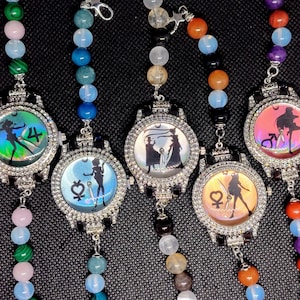 May include: Five beaded necklaces with watch-shaped pendants. Each pendant features a different silhouette design with a sparkling, crystal-like border. The beads are various colors, including pink, green, blue, orange, and purple.