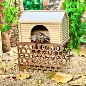 May include: A hermit crab in a decorative wooden house with a brown honeycomb-patterned base. The house has a light-colored roof and a round doorway. The crab is inside the house, with its legs visible.