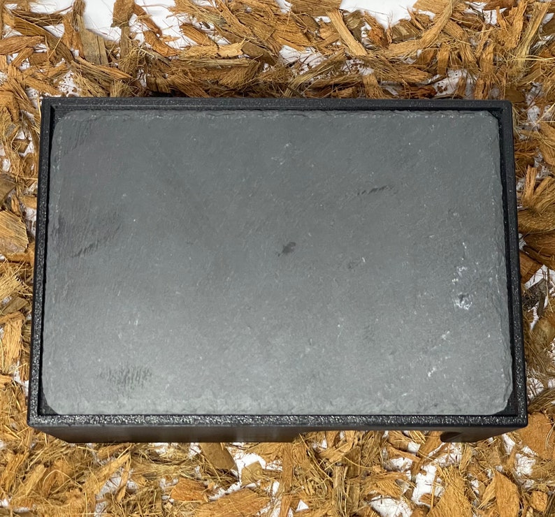 May include: A black slate serving tray with a raised edge. The tray is made of natural stone and has a rustic look.