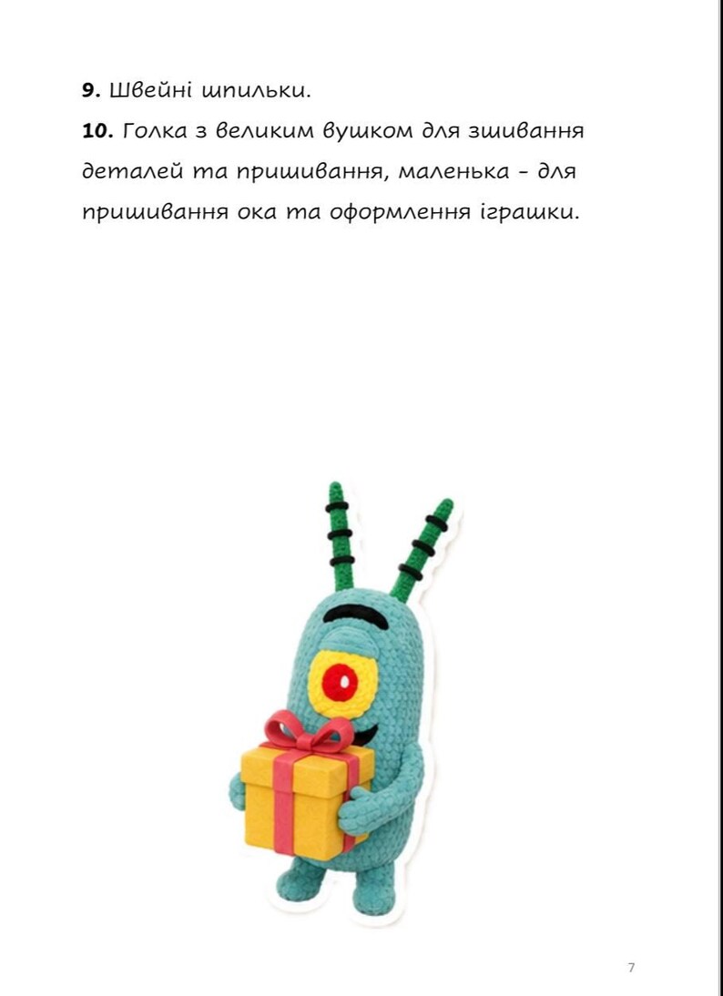 May include: A light blue crocheted character with two antennae, a single large yellow eye with a red pupil, and a black curved mouth. The character holds a yellow gift box with a red ribbon and bow. Text above reads 9. Швейні шпильки. 10. Голка з великим вушком для зшивання деталей та пришивання, маленька - для пришивання ока та оформлення іграшки.