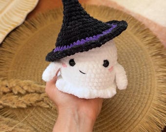 May include: A handmade white crochet ghost wearing a black witch hat with a purple band. The ghost has a smiling face with rosy cheeks and small arms. The ghost is a Halloween-themed item.