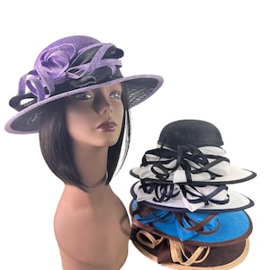 May include: A mannequin head wearing a purple and black hat with a large floral accent. A stack of four hats in various colors, including black, white, blue, and brown, with ribbon and mesh detailing, are displayed next to the mannequin.