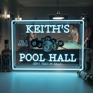 May include: A neon sign for a pool hall with the text "Keith's Pool Hall" and the phrase "Don't Touch My Balls!". The sign features a pool ball graphic and the words "Cold Beers" and "Good Times".