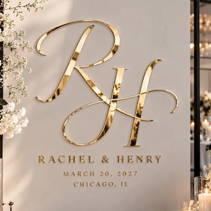 May include: A sign featuring large, gold, reflective script initials RH above the text RACHEL & HENRY, MARCH 20, 2027, CHICAGO, IL. The sign is displayed with white floral arrangements, pillar candles in glass holders, and a black guest book.