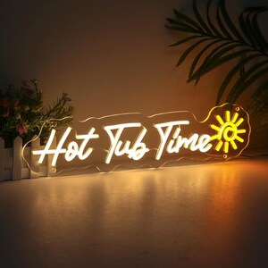 May include: A neon sign with the words "Hot Tub Time" in a cursive font. The sign is illuminated in a warm yellow color and features a sun design. The sign is mounted on a clear acrylic backing.