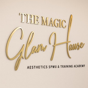 Pode incluir: Logotipo com letras 3D douradas. As palavras "THE MAGIC Glam House" são exibidas, com "AESTHETICS SPMU & TRAINING ACADEMY" abaixo em uma fonte menor. O fundo é de cor branco-sujo neutro.
