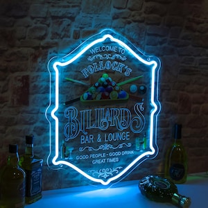 Könnte beinhalten: Blau leuchtendes Neon-Schild für "Pollock's Billiards Bar & Lounge" mit Billardtisch-Grafik. Der Schriftzug lautet "Good People - Good Drink - Great Times". Mehrere Flaschen sind im Vordergrund zu sehen, vor einer Backsteinmauer.