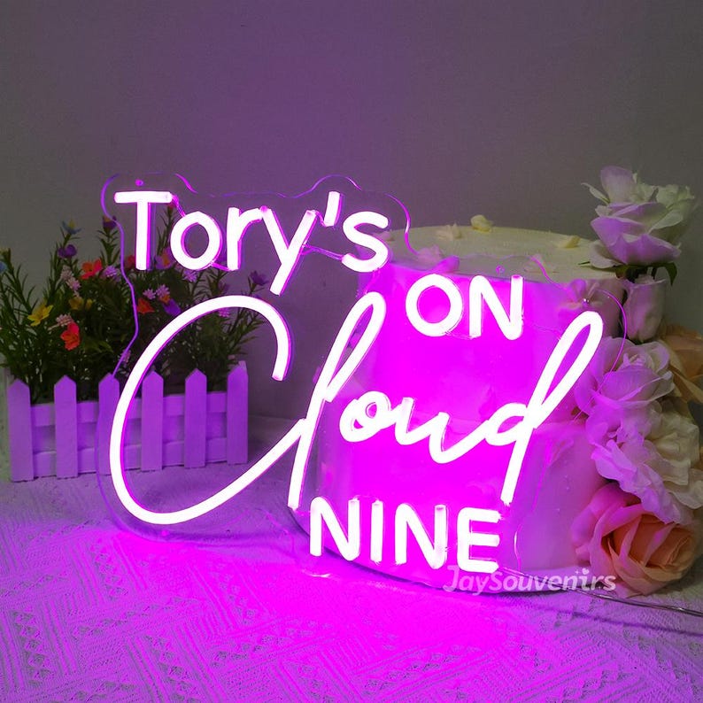 May include: A pink neon sign with white lettering that reads "Tory's On Cloud Nine".