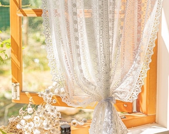 May include: White lace curtain with a delicate floral pattern and scalloped edges. The curtain is hung in a window with natural light streaming through.