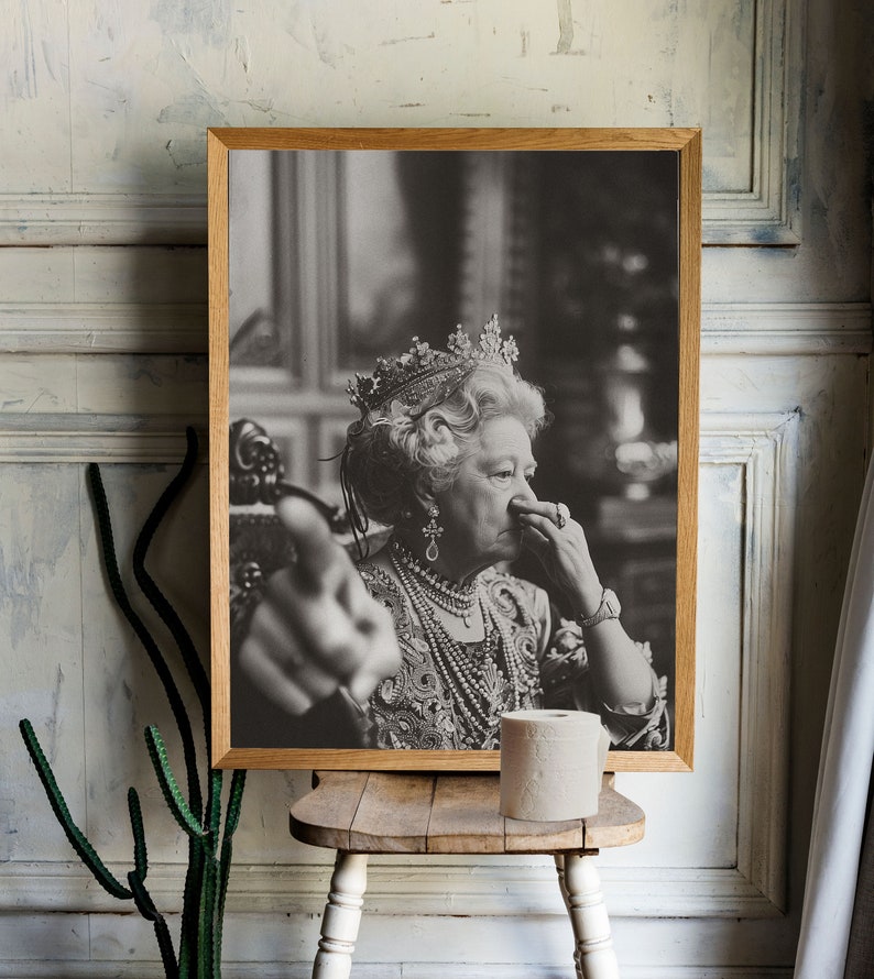 May include: A black and white photo of a woman wearing a crown and a pearl necklace. She is holding her nose with her right hand and pointing with her left hand. The photo is framed in a wooden frame.