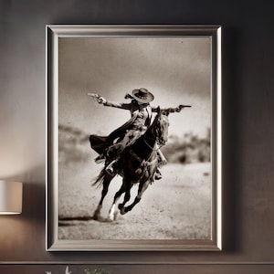 May include: A black and white photograph of a woman wearing a cowboy hat and riding a horse. She is holding a gun in her right hand and is looking to the right. The horse is running and the woman is leaning forward.