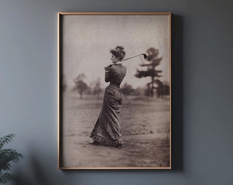 Puede incluir: Una fotografía vintage en blanco y negro de una mujer con un vestido largo jugando al golf. Ella sostiene un palo de golf y está en medio de su swing. La foto está enmarcada en un marco de madera.