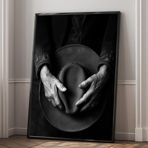 Pu&ograve; includere: Una fotografia in bianco e nero di mani che tengono un cappello a tesa larga. Il cappello &egrave; fatto di un materiale scuro e ha una texture liscia. Le mani della persona sono rugose e mostrano segni di et&agrave;.