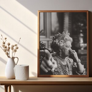 May include: A black and white photo of a woman wearing a crown and a pearl necklace. She is looking at the camera and has her hand raised in a gesture of pointing.