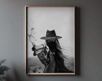 Pode incluir: Uma fotografia a preto e branco de uma pessoa usando um chapéu de aba larga e uma máscara, segurando uma arma. A pessoa está em pé num ambiente desértico.
