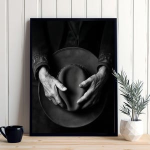 Pu&ograve; includere: Fotografia in bianco e nero di mani che tengono un cappello a tesa larga. Il cappello &egrave; fatto di un materiale scuro e ha una superficie leggermente strutturata. Le mani della persona sono rugose e mostrano segni di et&agrave;.